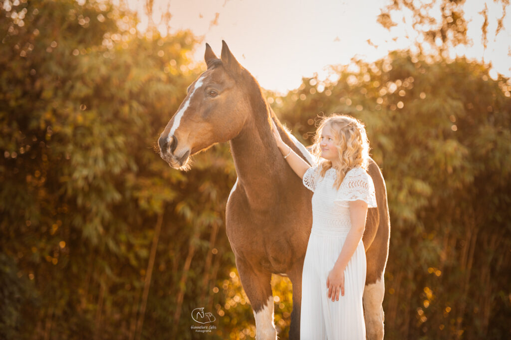 Paard met vlekken met jong meisje in witte jurk voor een lentefeest die samen in dezelfde richting kijken.