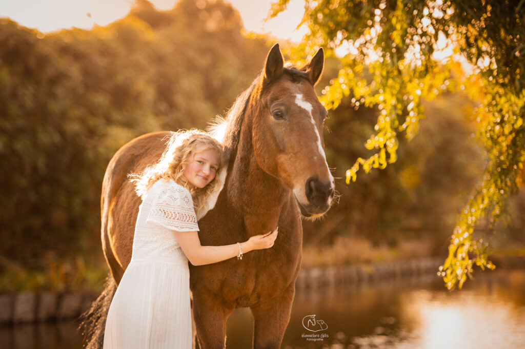 Paard met witte en bruine vlekken met jong meisje in witte jurk voor een lentefeest die knuffelen tijdens een professionele fotoshoot.